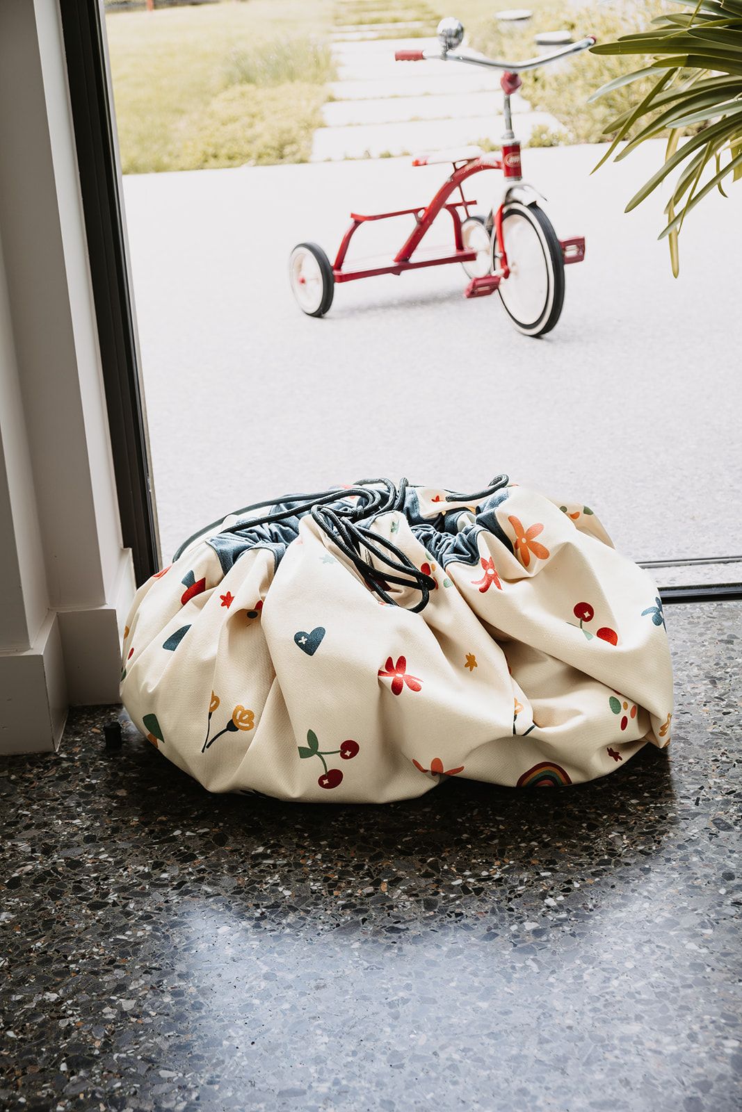 funny days toy storage bag and playmat, closed bag in front of the window, tricycle outside