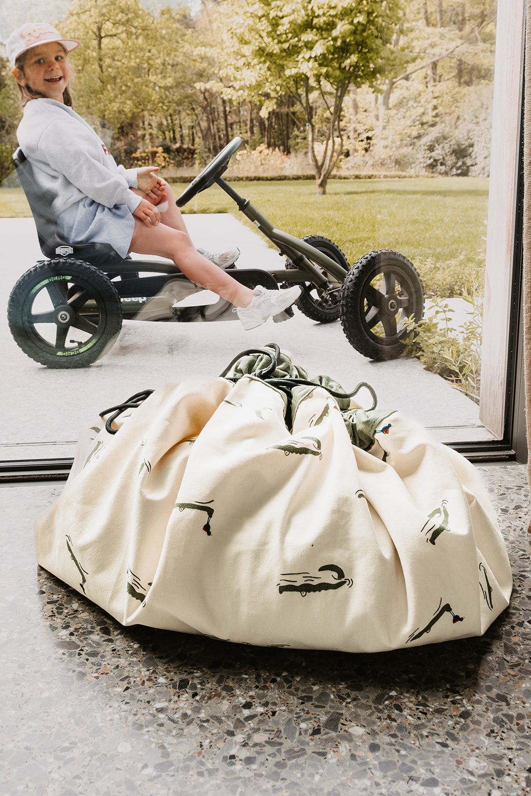 croco toy storage bag and playmat, on floor at the window, child is playing outside with go car