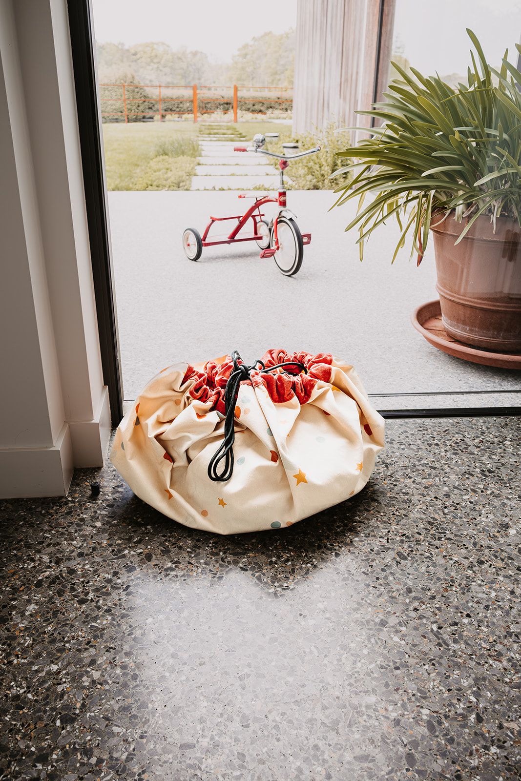 circus toy storage bag and playmat, closed bag standing in front of the window, garden and tricycle