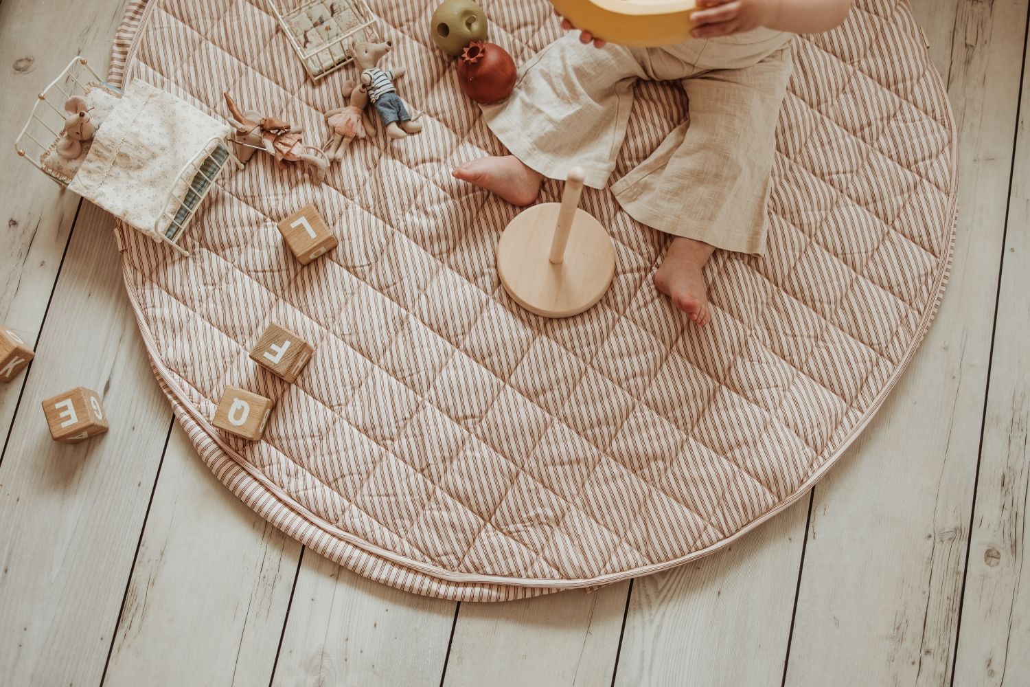 soft stripes brown organic babymat, child is sitting on the mat, playing with a banana, wooden toys, mouse cuddles