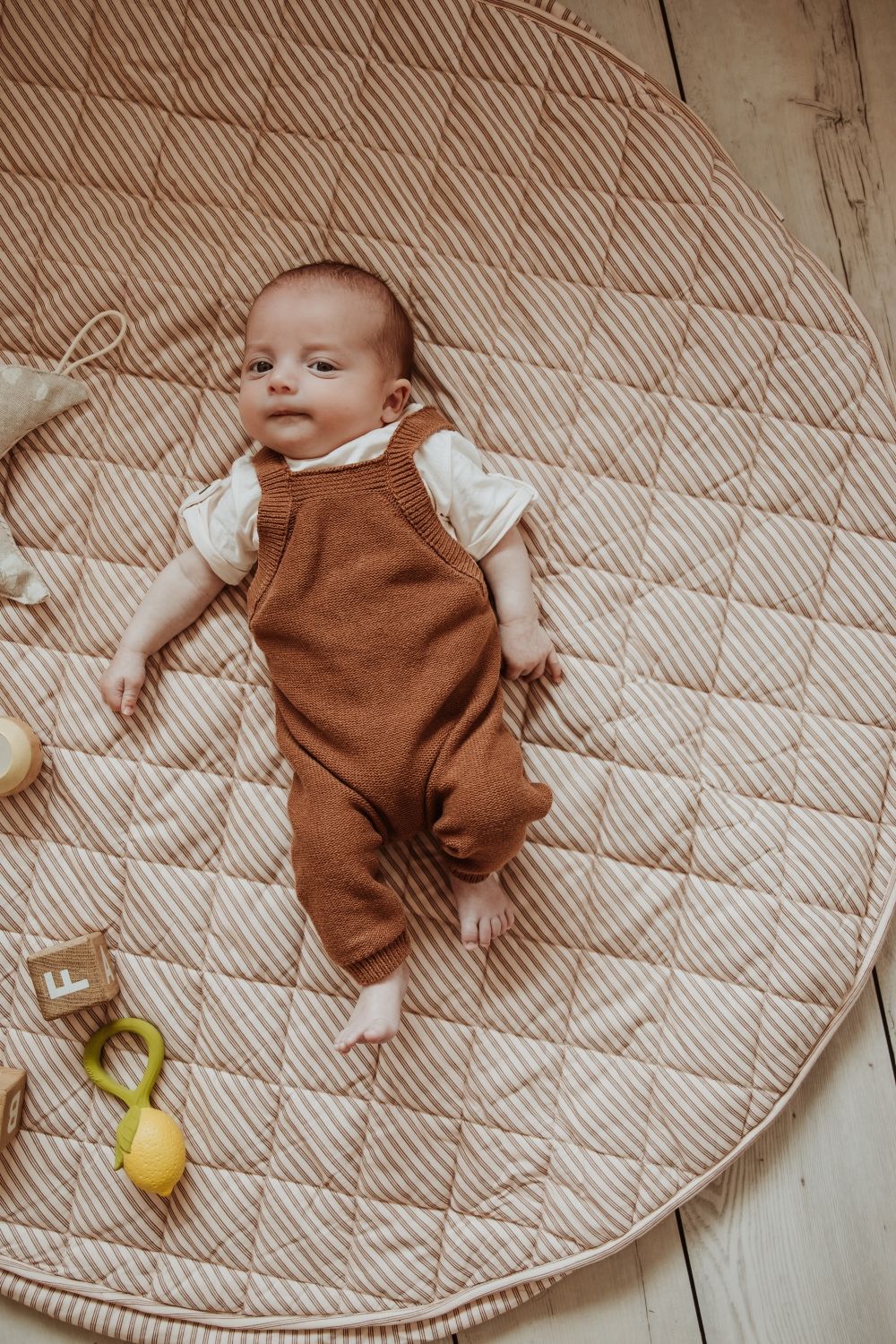 soft stripes brown organic babymat, little baby is lying on the mat, wooden blocks and lemon toy