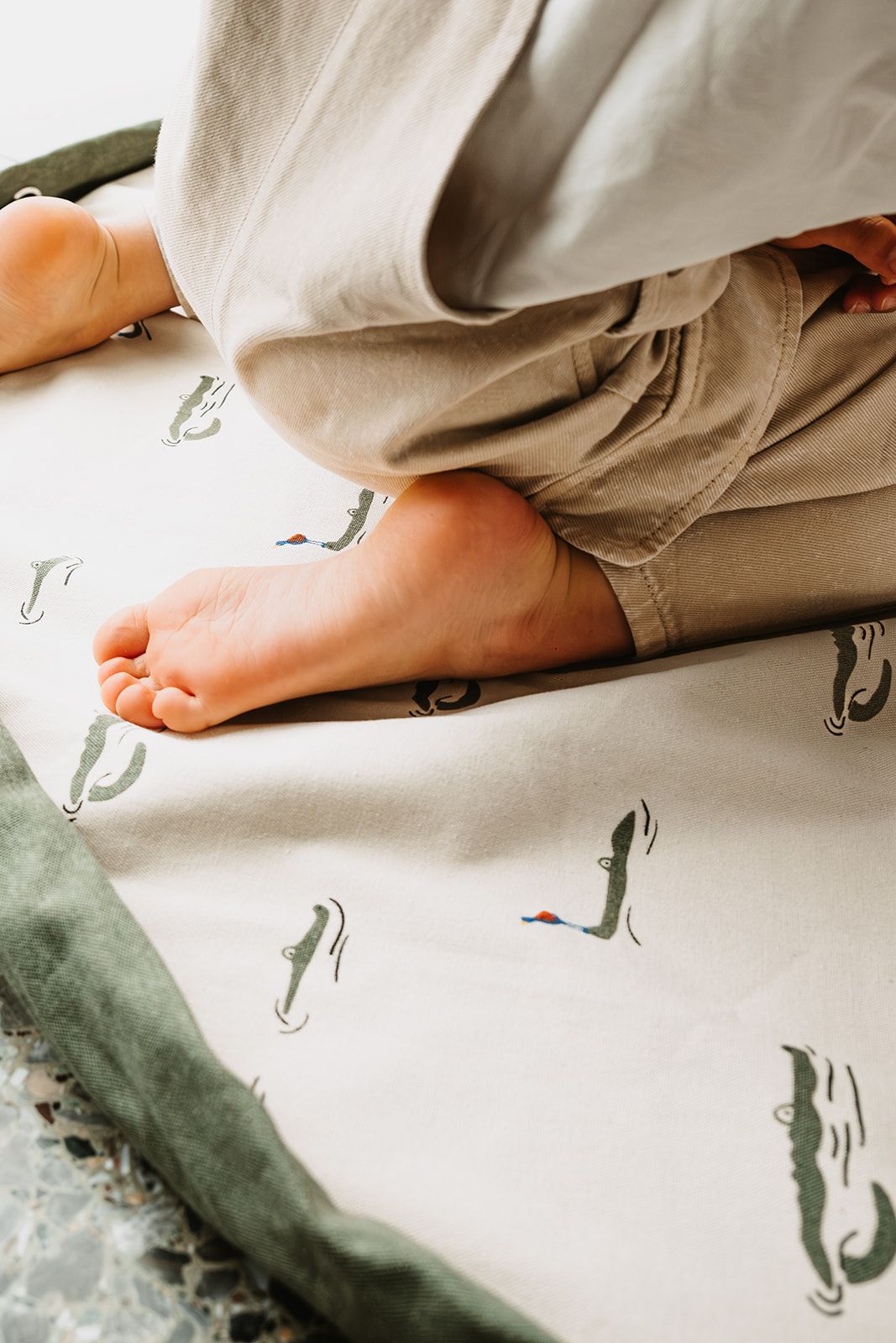 croco toy storage bag and playmat, child is sitting on the mat, little feet