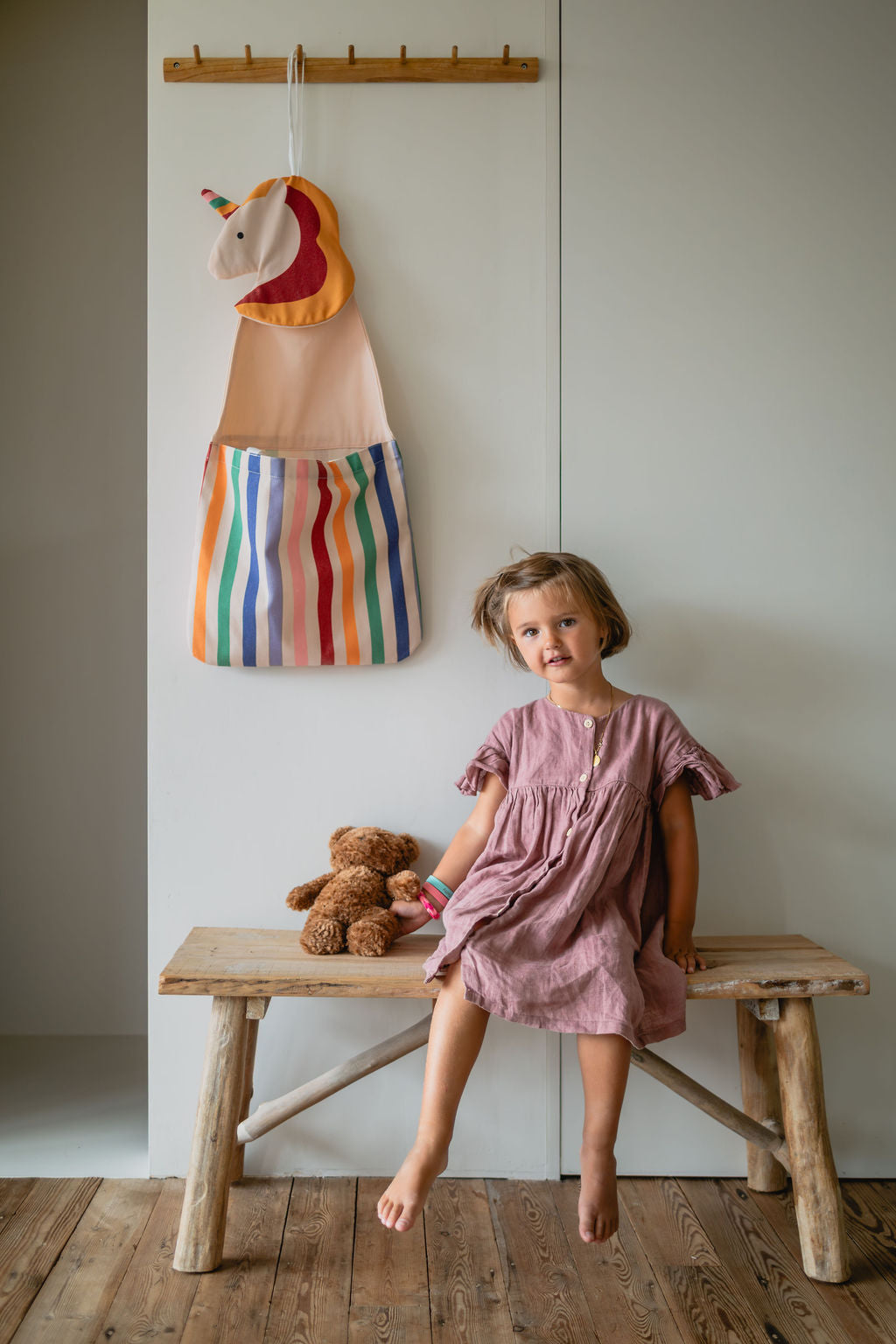 toto unicorn, hanging on the wall, child is sitting on a wooden bench, holding a cuddle bear
