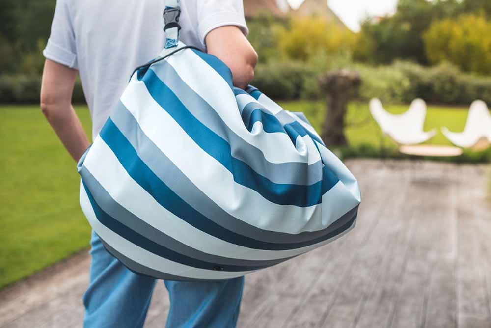 outdoor storage bag blue/green stripes, person carrying closed bag while standing on the terrace in the garden