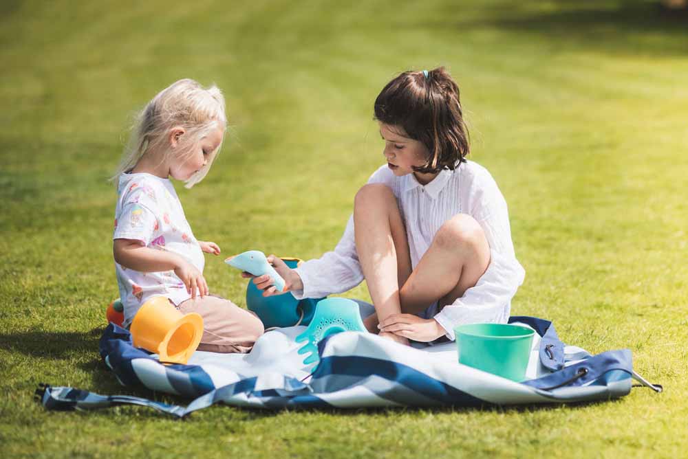 outdoor storage bag blue/green stripes, children sitting on open bag in garden, playing and talking