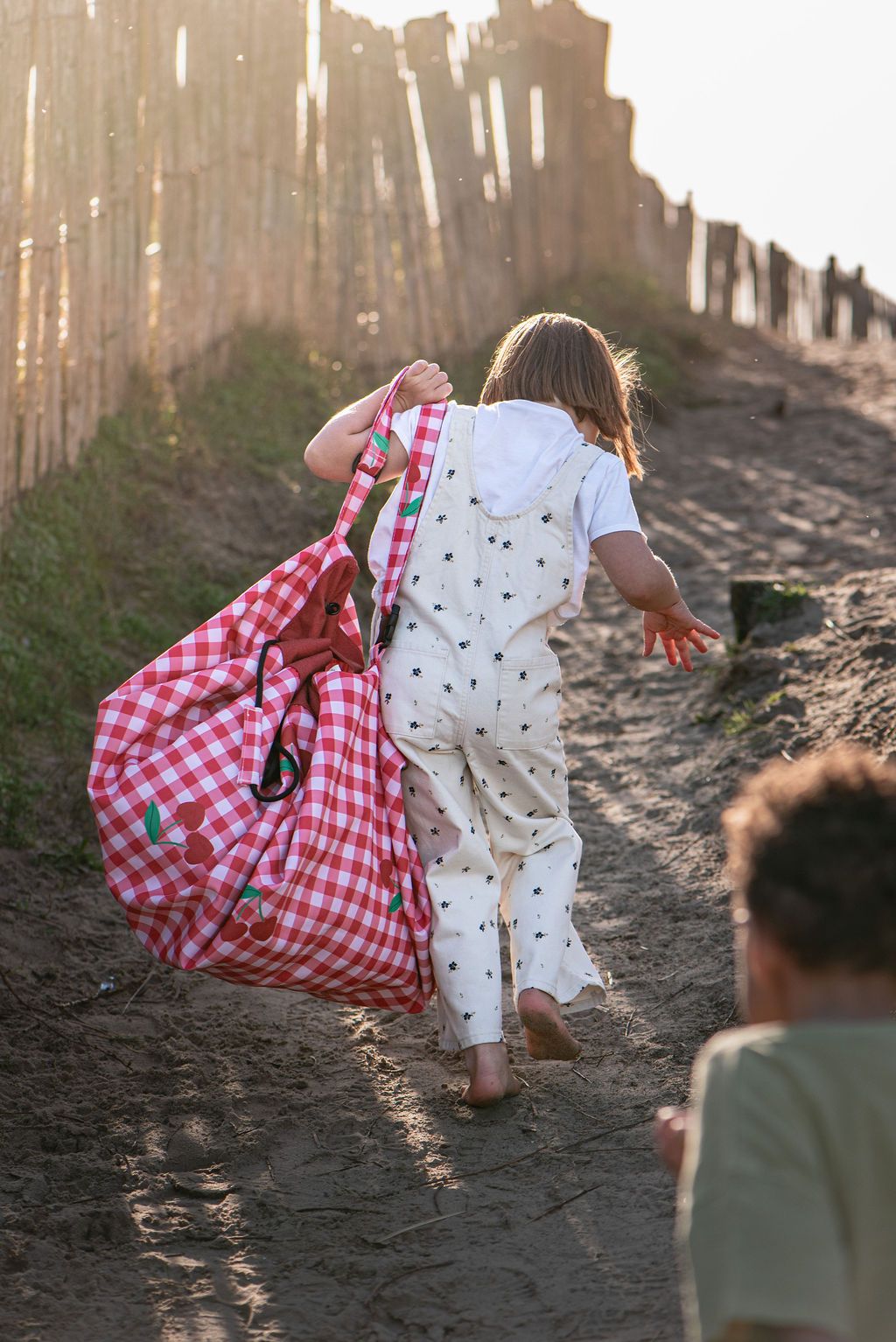 pic nic outdoor playmat, children are walking in the sand while holding the closed bag on the shoulders