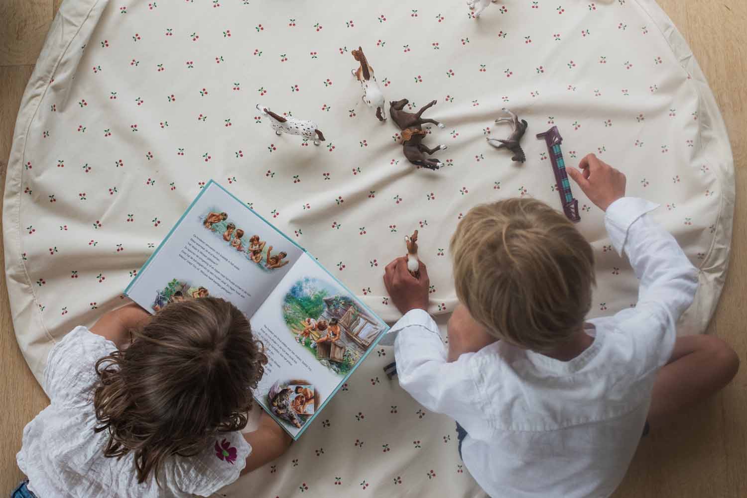 cherry cherry toy storage bag, open on floor, children playing and reading a book