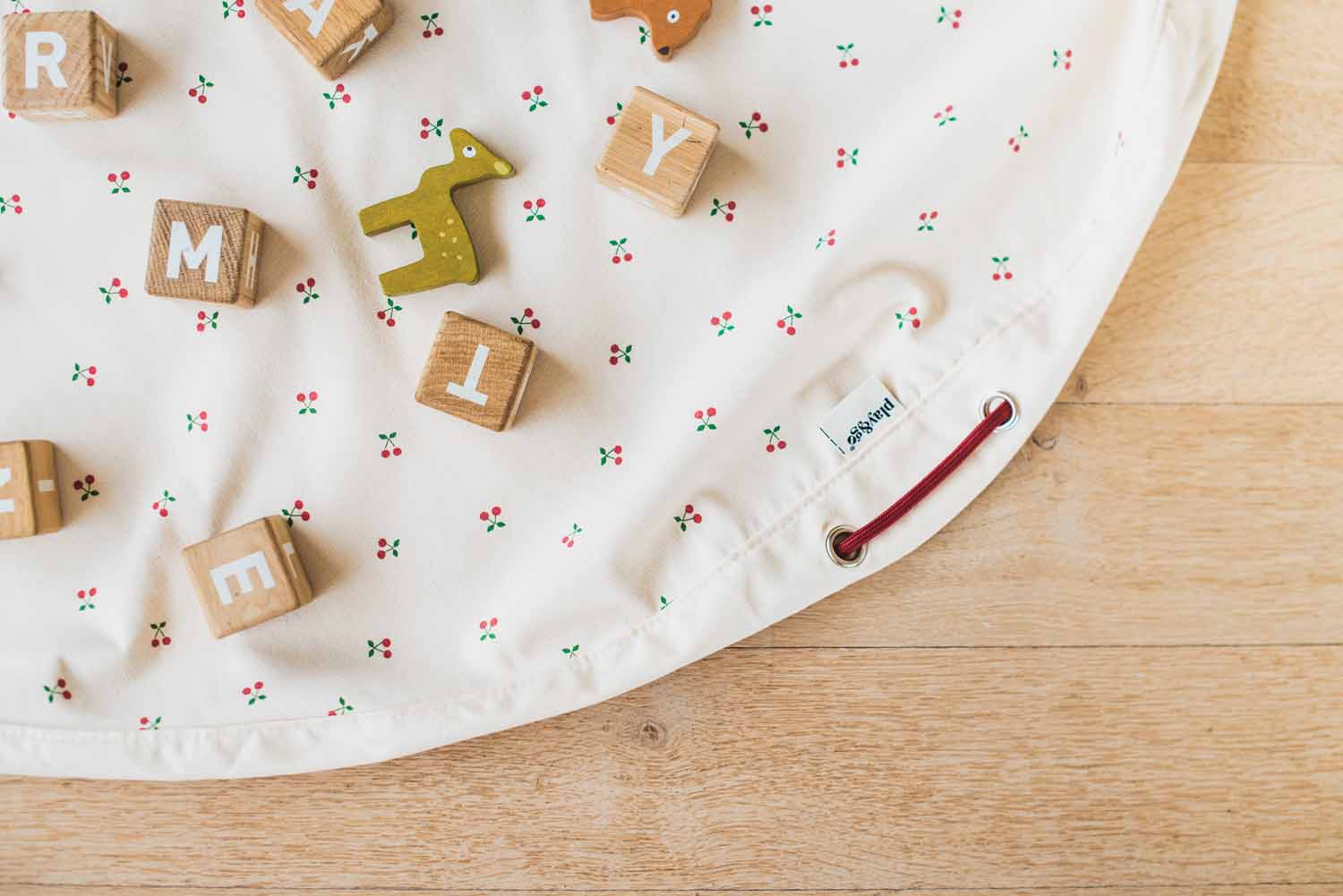 cherry cherry toy storage bag, open on floor, wooden deer and blocks on the open mat