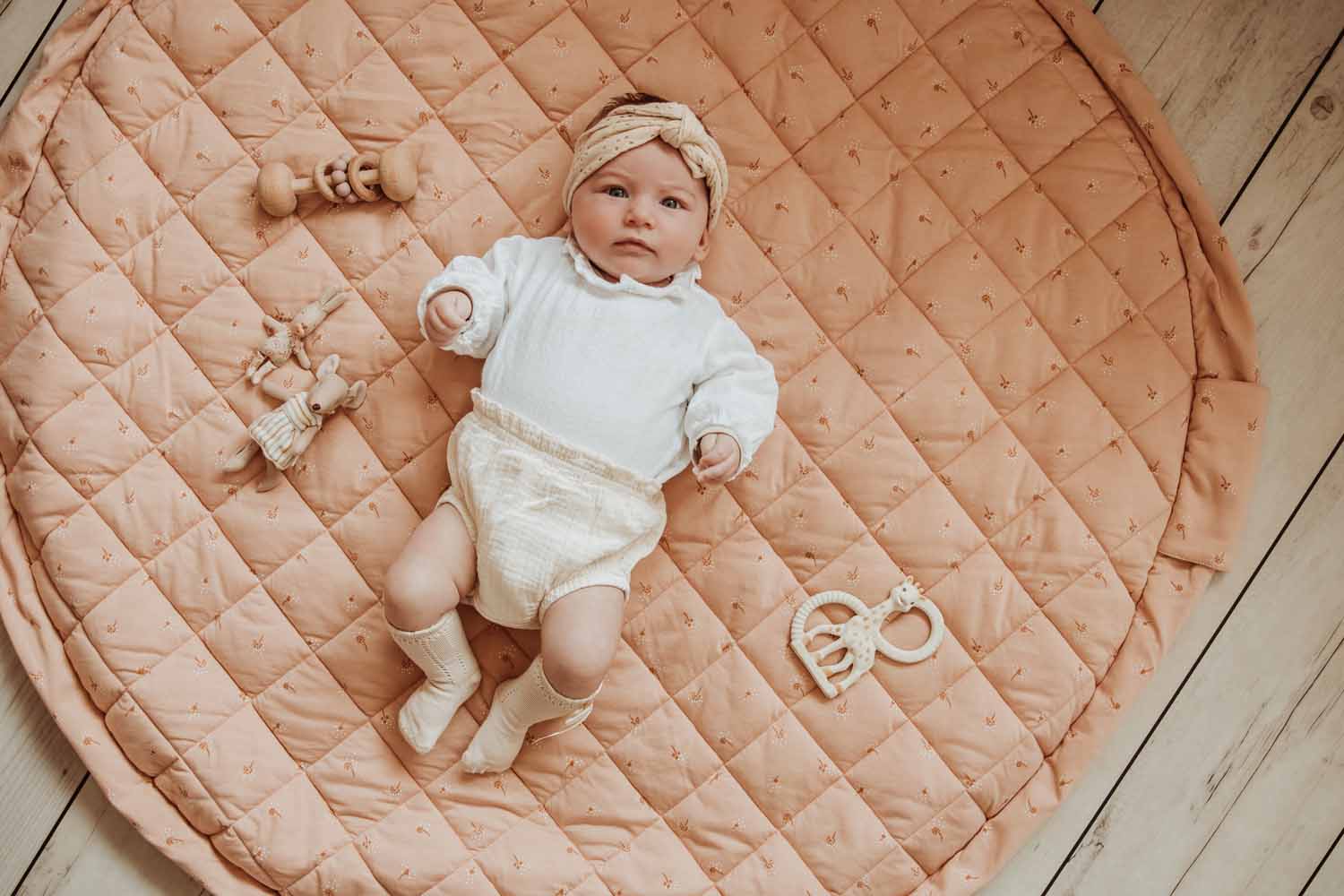 Fleuri organic babymat, baby lying on the mat with toys, looking into the camera
