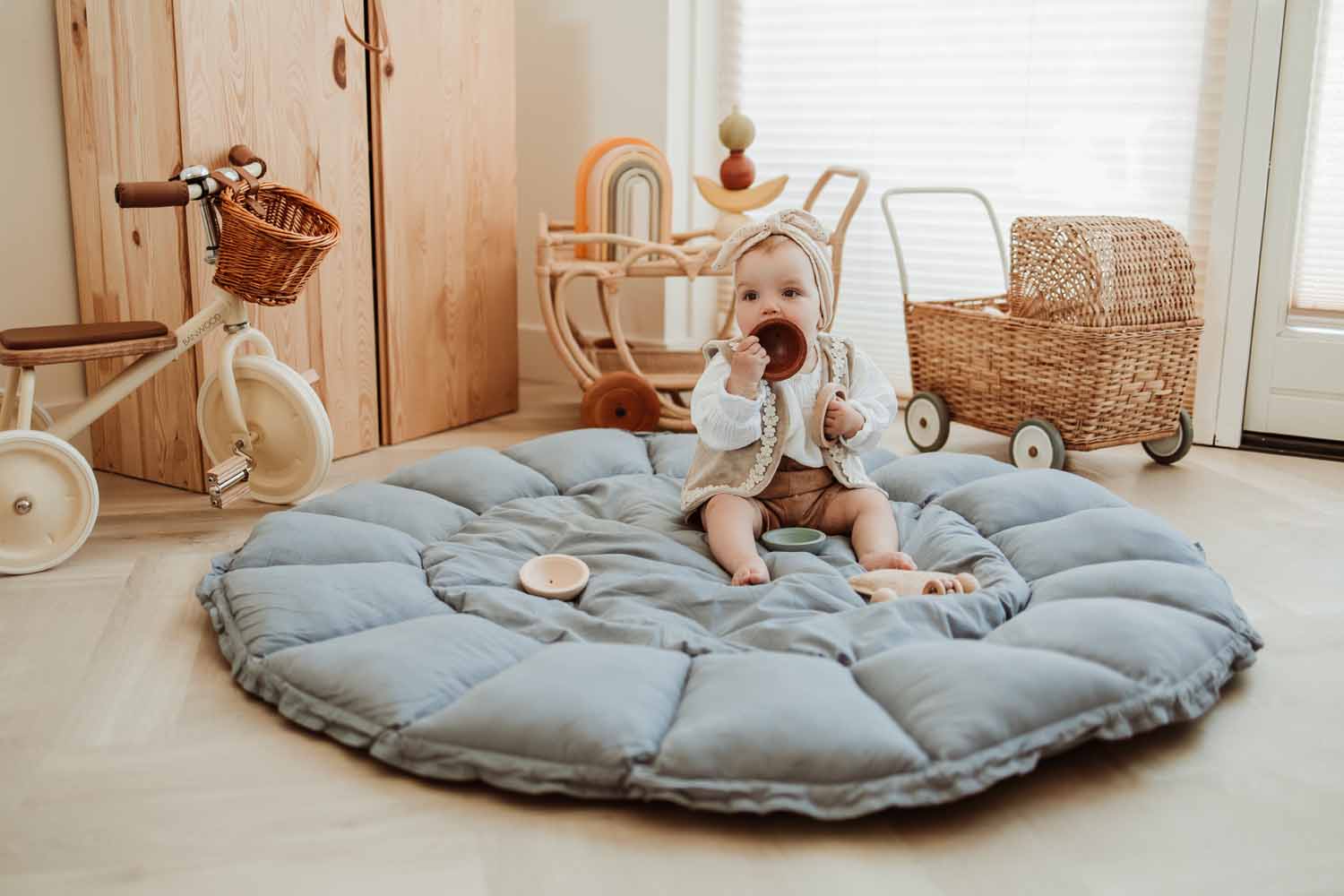 Bloom dusty blue organic babymat, open on floor in kidsroom, child sitting on mat, playing, tricycle and baby carriage