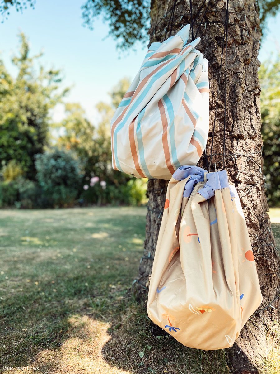 Play&Go outdoor storage bag and play mat, one bag with stripes, one with little icons, bags hanging on tree