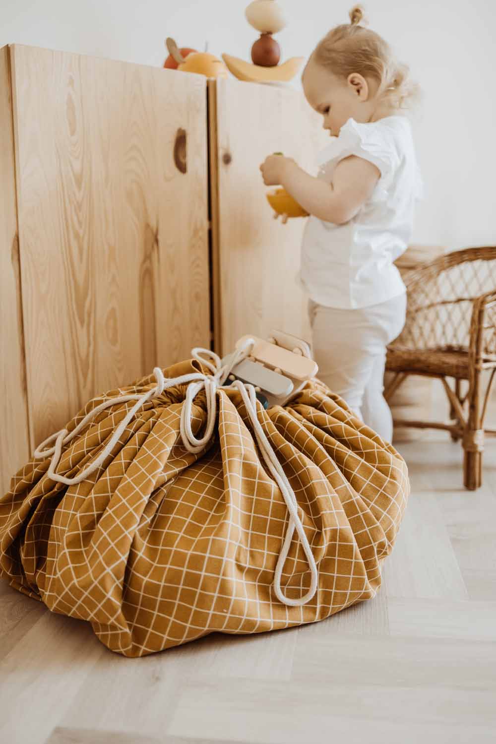 closed organic grid mustard storage bag, on floor in kidsroom, child playing with wooden toys, wooden closet