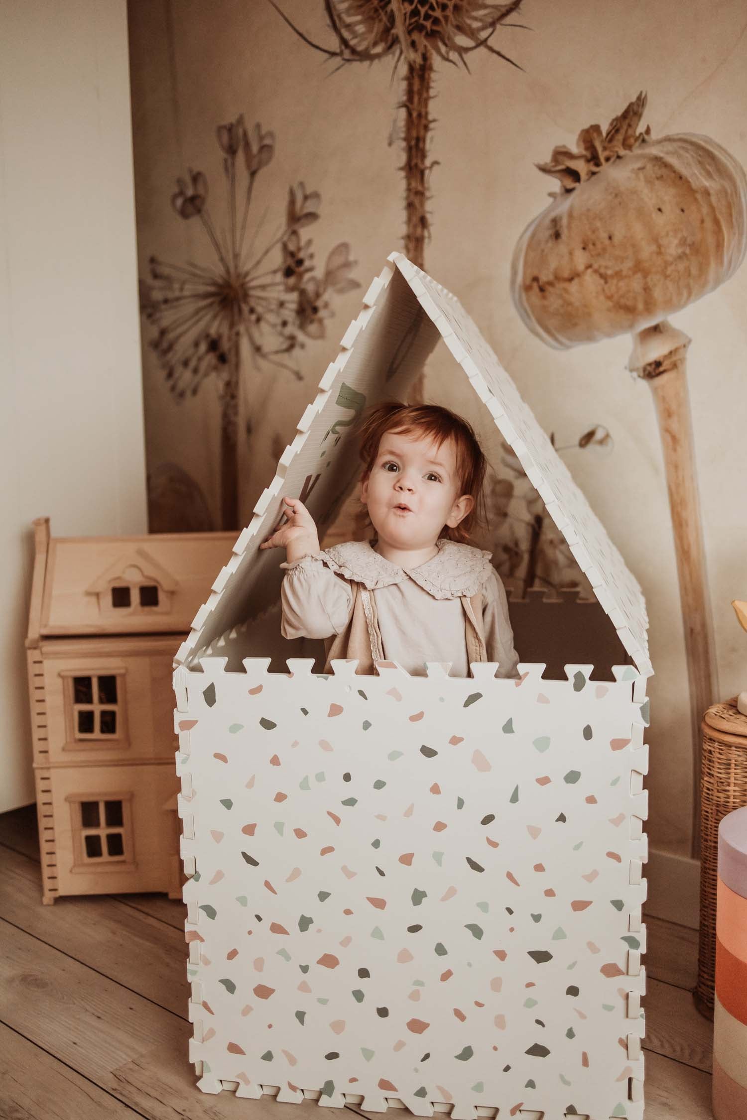child standing in cosy house made of terrazzo puzzlemat, looking outside